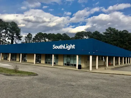 Blue exterior of SouthLight Raleigh Hub, a treatment center in Raleigh, surrounded by trees and cloudy sky.
